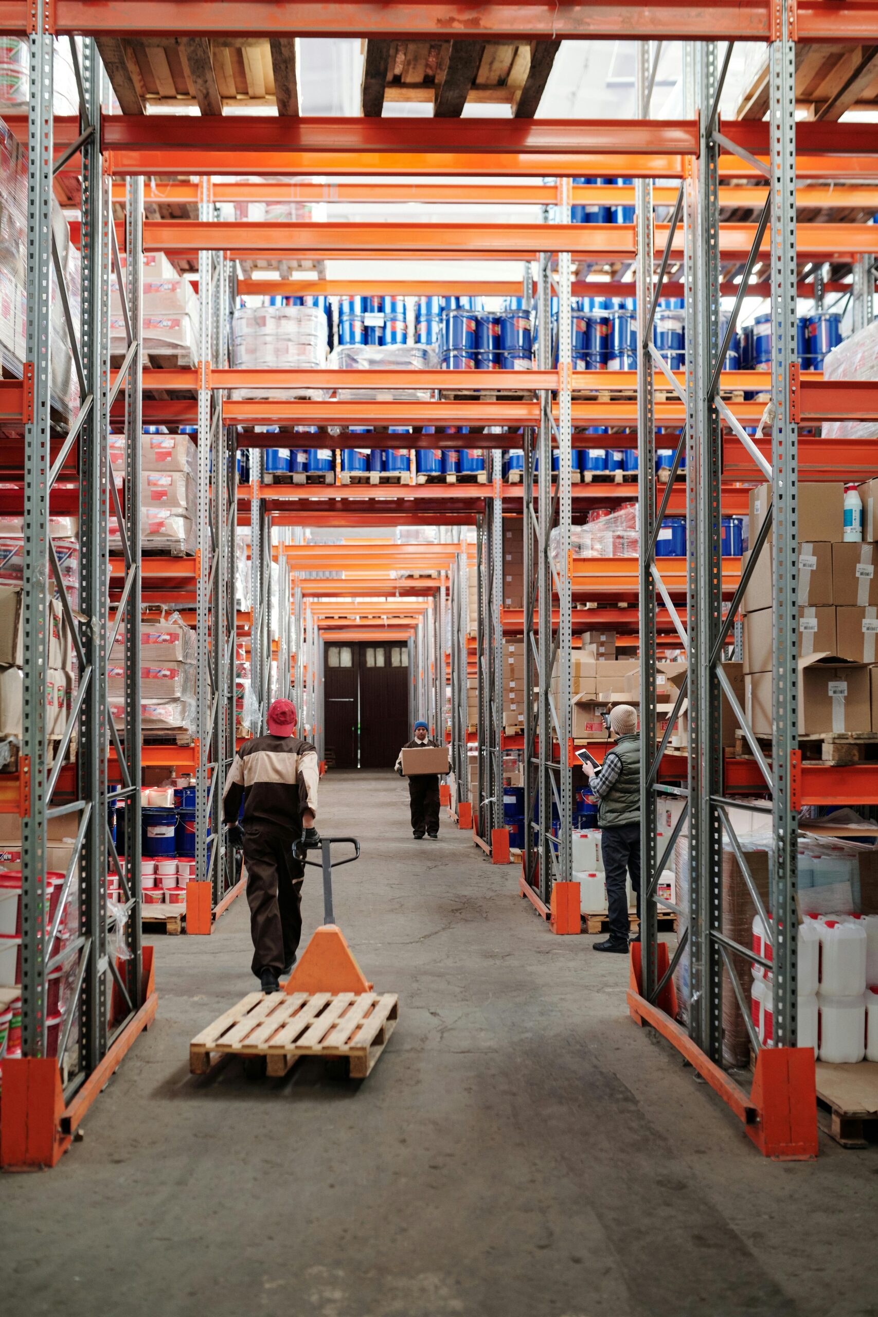 Home Workers arrange inventory on shelves in a large industrial warehouse.